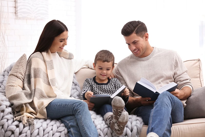 Family sitting in living room reading together, American Standard Furnaces Heat Pumps