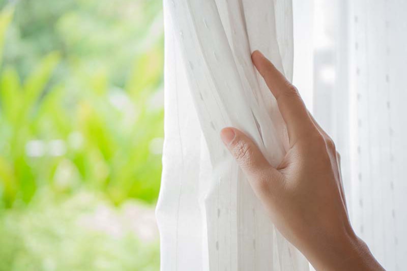 Woman's hand opening curtains in the bedroom in the spring, Spring Money-Saving Tips | AC Maintenance | Port Orchard, WA