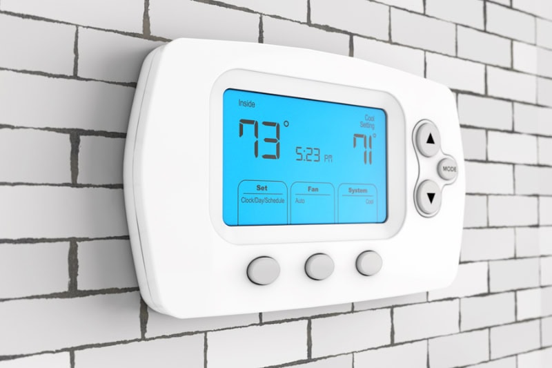 Thermostat Settings: On vs. Auto. Photo of a digital thermostat mounted on the wall with a blue light.
